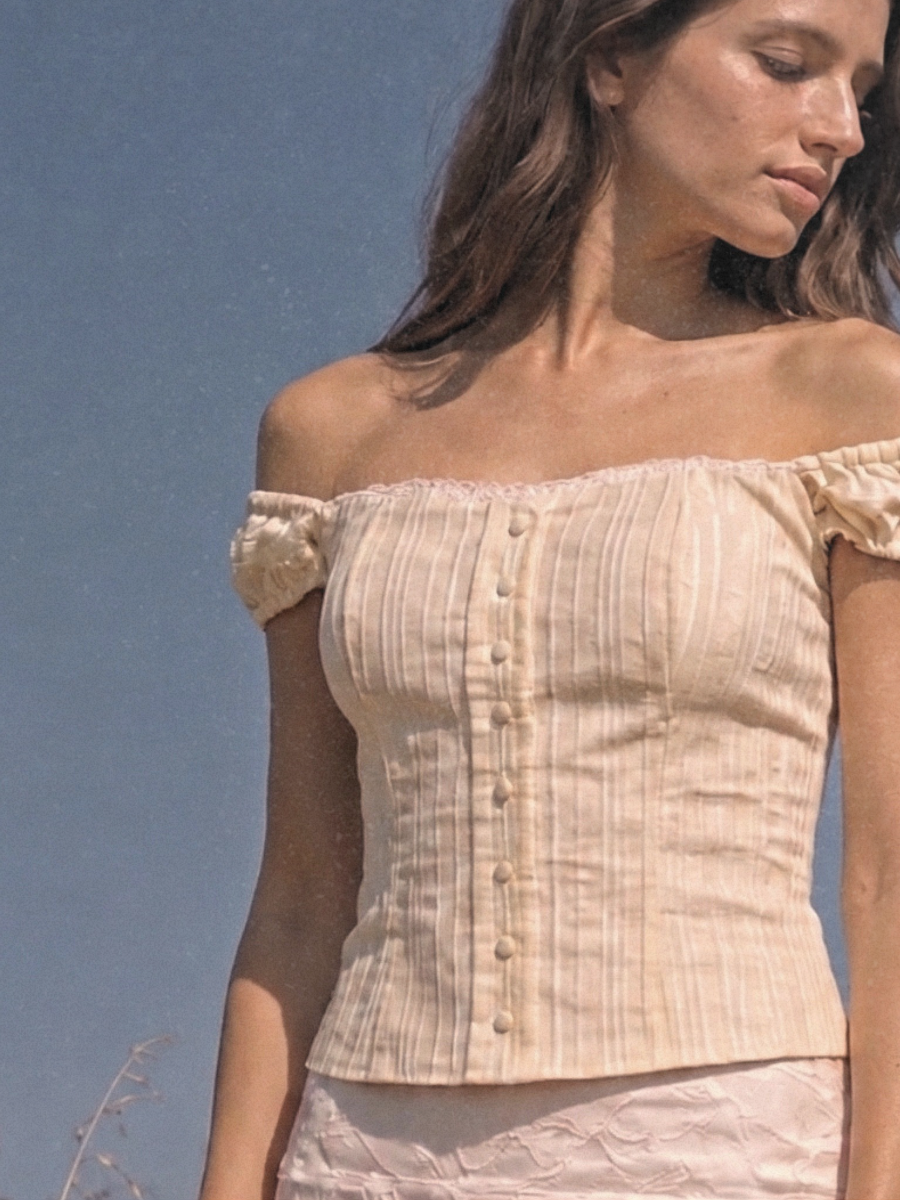 Feminine wear, feminine outfit, romantic vibe aesthetic outfit, cottagecore wear, elegant women clothing brand — Close-up of a woman in a delicate cream off-shoulder button-front top paired with a soft floral skirt, showcasing the romantic and feminine details of the outfit.